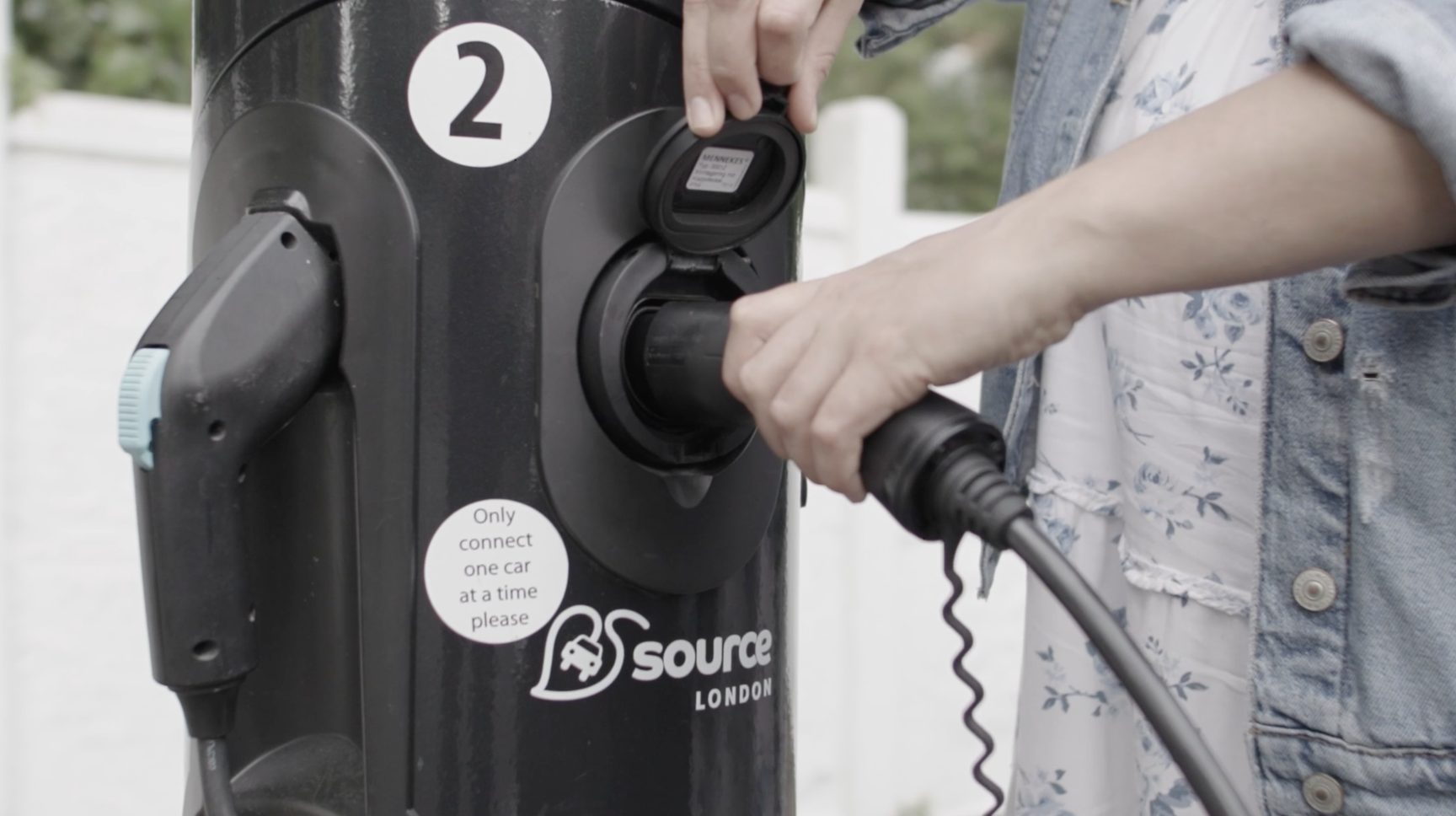 Image shows woman charging an EV using the Source London on street EV charging station