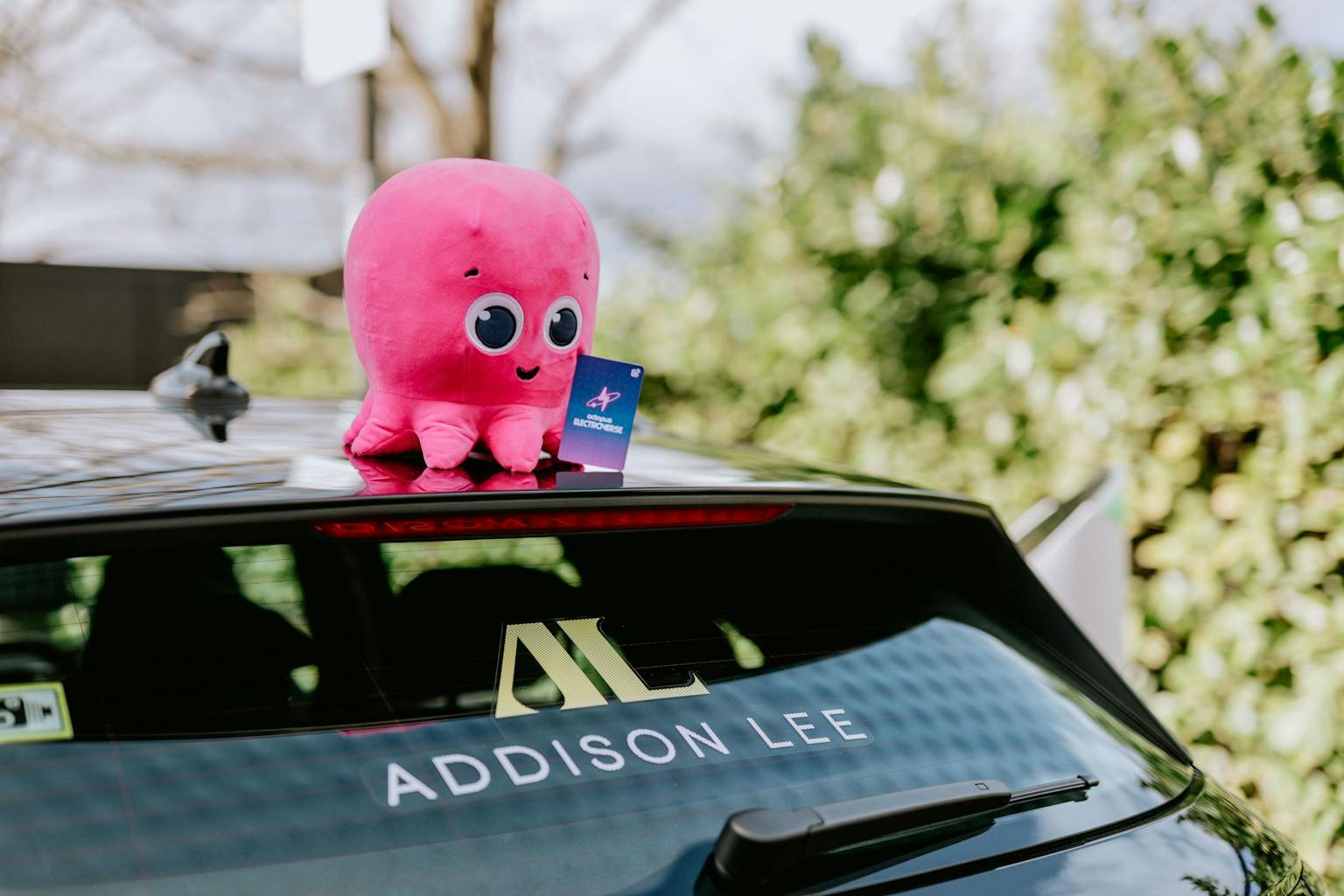 Octopus Energy mascot, Constantine, sits on top of Addsion Lee taxi holding an Octopus Electroverse charging card